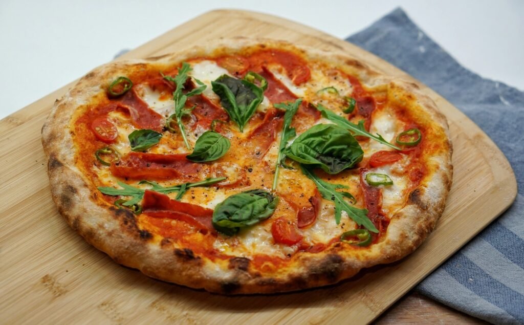 Freshly baked pizza with tomato, mozzarella, basil, arugula, and green chili on a wooden board.