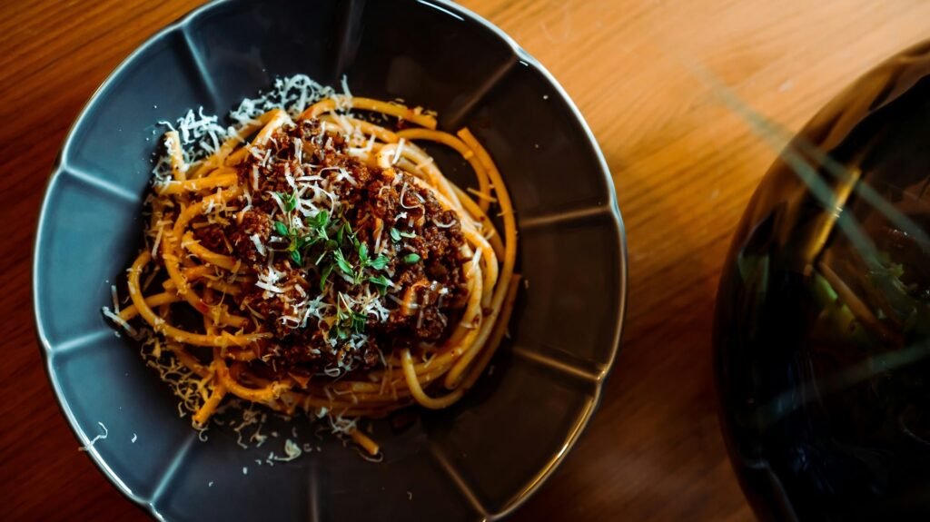 A plate of pasta topped with Bolognese sauce, grated cheese, and herbs in a dark bowl.