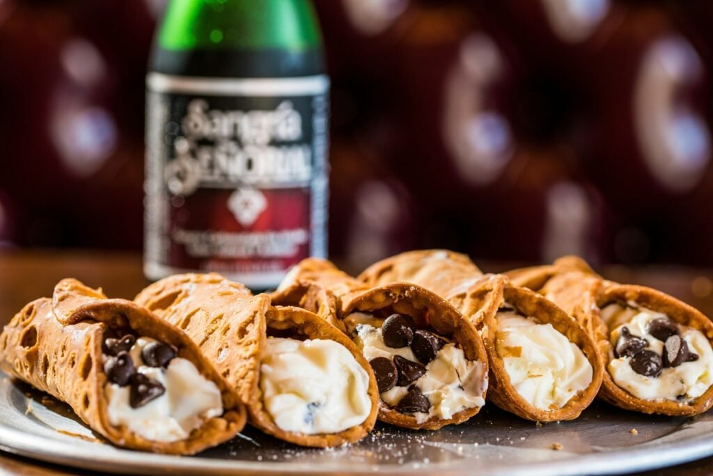 A plate of cannoli filled with cream and chocolate chips, with a drink in the background.