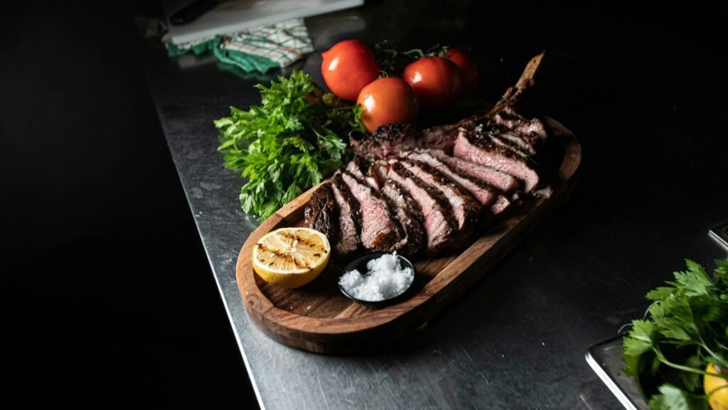 Sliced Florentine steak served on a wooden board with lemon, salt, tomatoes, and fresh parsley.