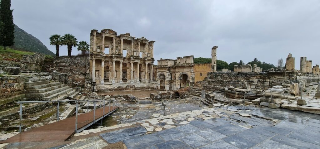 Ancient ruins of the Library of Celsus in Ephesus (Izmir), with stone structures and cloudy skies.