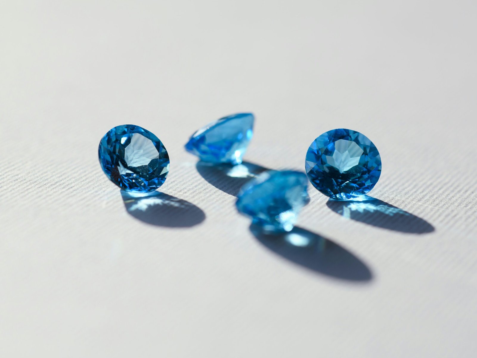 Four round-cut blue gemstones resting on a light surface with soft shadows.