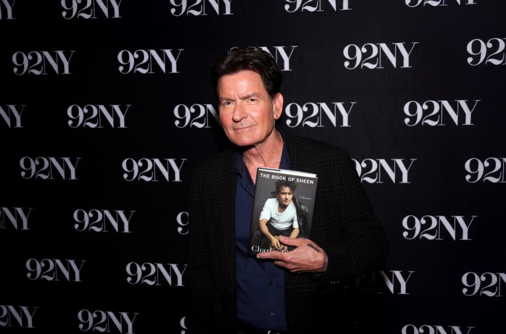 Charlie Sheen holding a copy of his memoir The Book of Sheen at a promotional event.