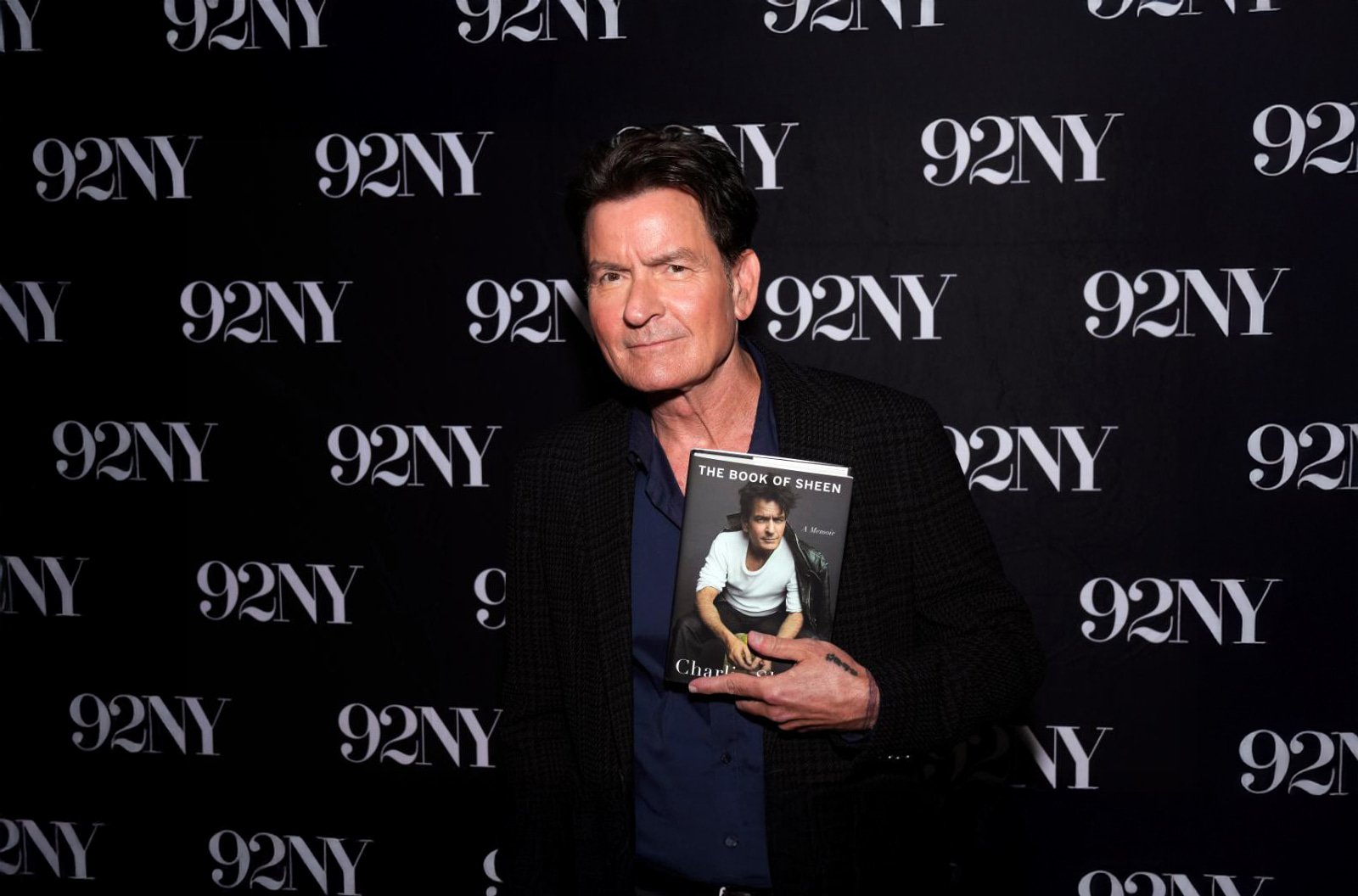 Charlie Sheen holding a copy of his memoir The Book of Sheen at a promotional event.